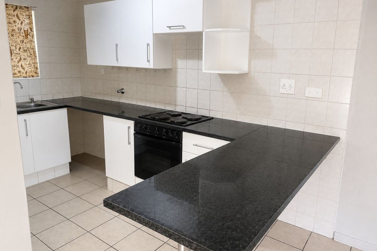 A clean, functional kitchen featuring granite countertops, built-in oven and hob, ample cabinetry, and a convenient breakfast bar for casual dining.