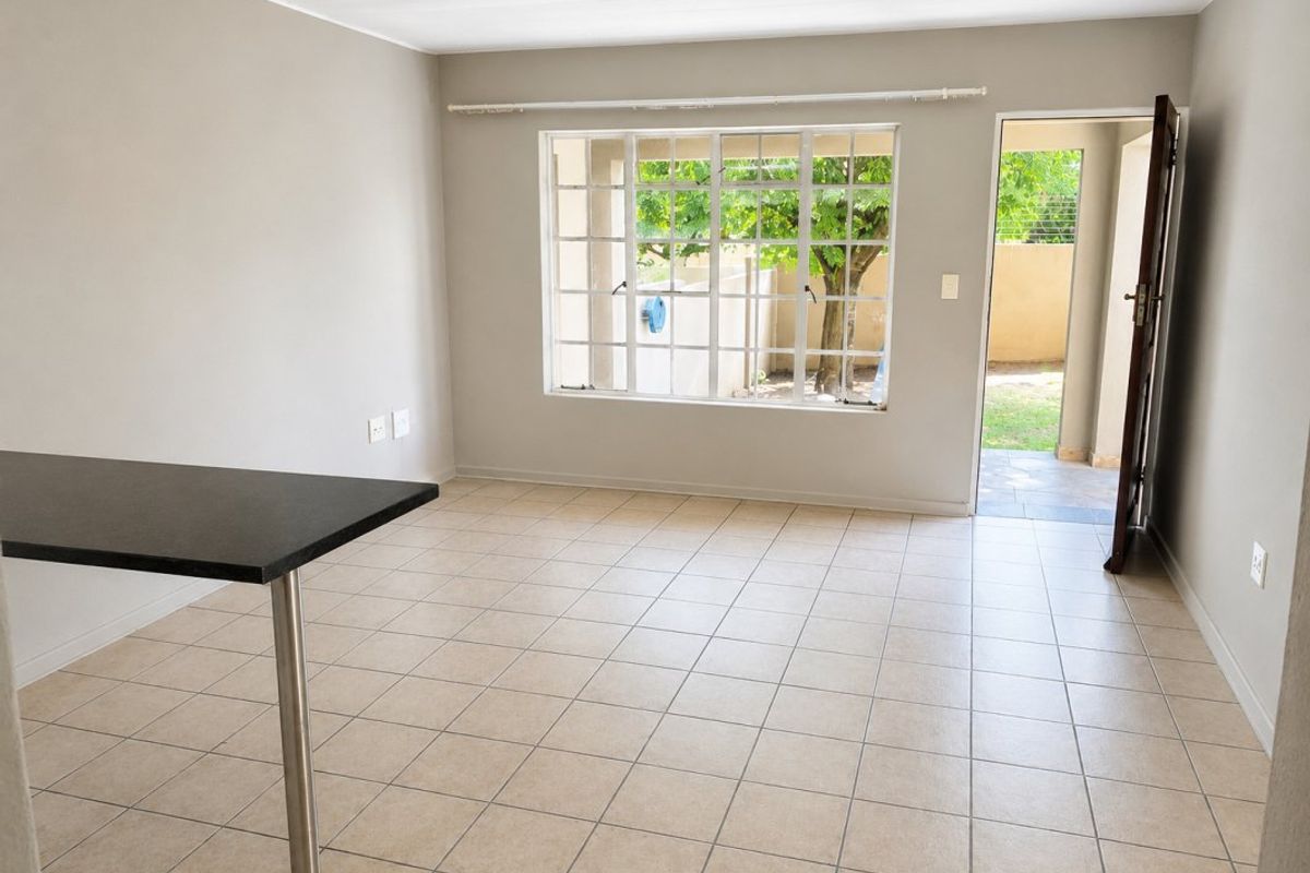An open-plan living area featuring tiled flooring, a breakfast bar, and direct access to the rear garden through a glass-paned door.