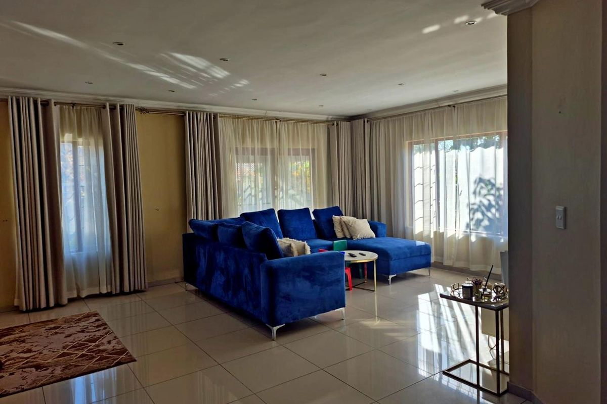 Spacious living room featuring large windows, neutral tiled flooring, and recessed downlighting, creating a bright and open atmosphere.