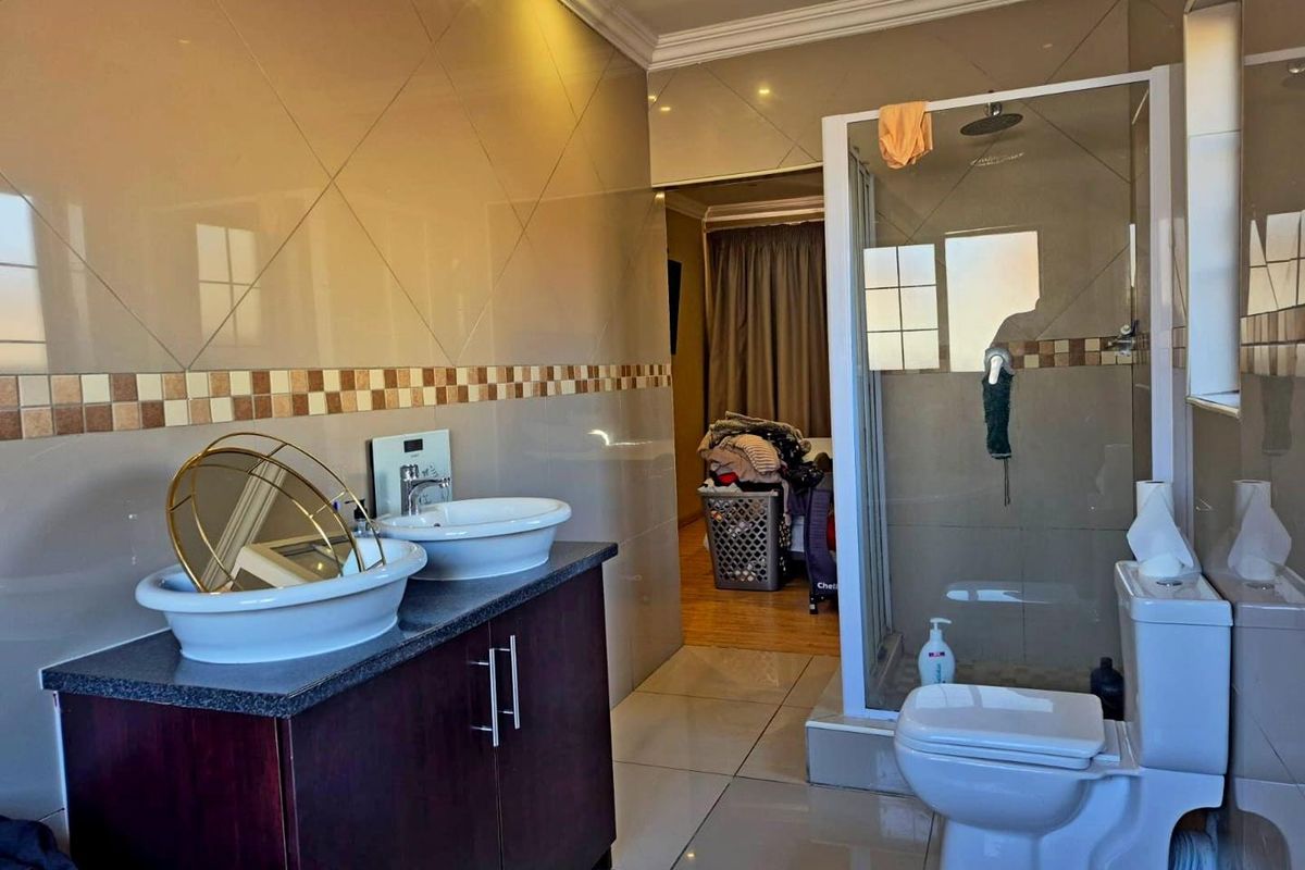 A modern bathroom featuring a double vanity with vessel sinks, a glass-enclosed shower, and neutral wall and floor tiling.