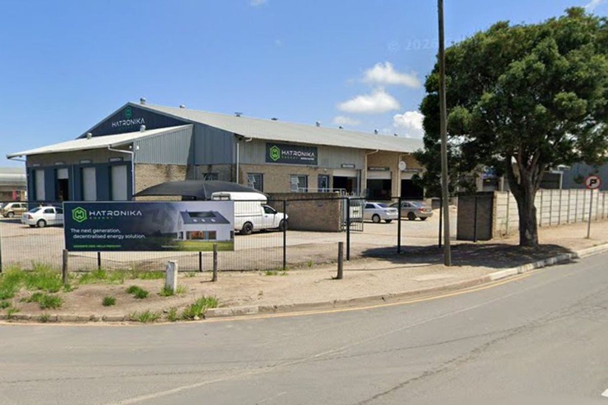 Front view of an industrial warehouse facility featuring metal cladding, multiple roller shutter doors, and a paved yard area enclosed by perimeter fencing.
