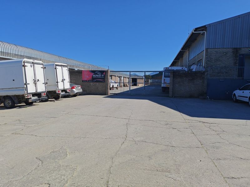 Industrial property exterior featuring a concrete yard, metal security gate, and brick boundary wall with corrugated metal warehouse structures.