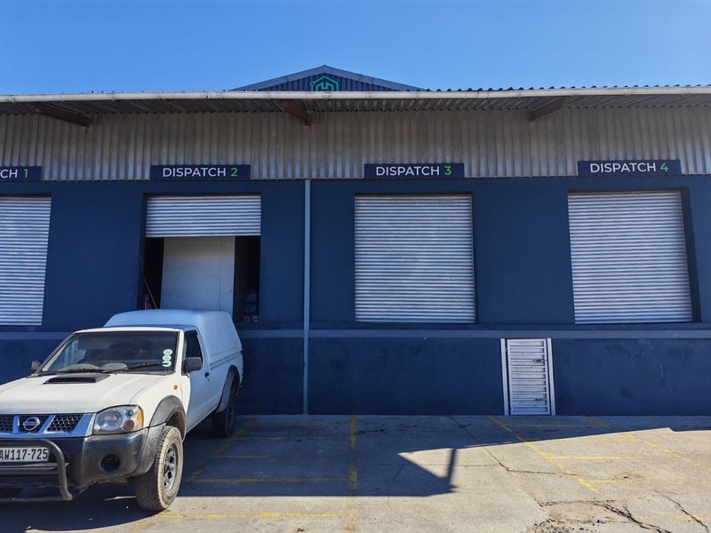 Industrial warehouse exterior featuring multiple dispatch bays with roller shutter doors and a concrete loading area.