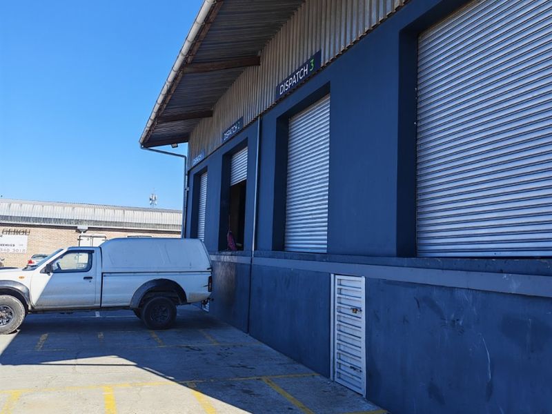 Industrial warehouse exterior featuring multiple roller shutter dispatch bays, concrete loading area, and clear signage for logistics operations.