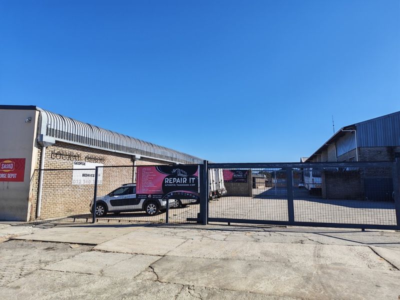 Industrial property exterior featuring a secure metal sliding gate, brick facade, and corrugated metal roofing with a concrete driveway.