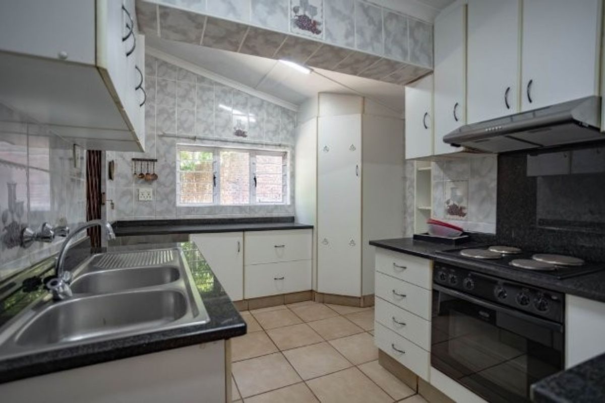 A functional kitchen featuring granite countertops, built-in oven and hob, extractor fan, and ample storage cabinetry with tiled splashbacks and flooring.