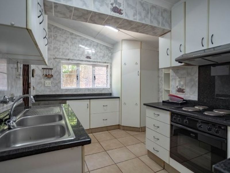 A functional kitchen featuring granite countertops, built-in oven and hob, extractor fan, and ample storage cabinetry with tiled splashbacks and flooring.