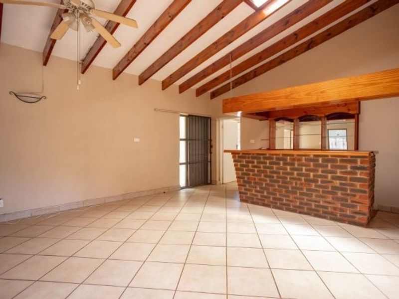 Spacious living area featuring exposed timber ceiling beams, tiled flooring, and a built-in brick bar, offering a versatile layout for entertainment.