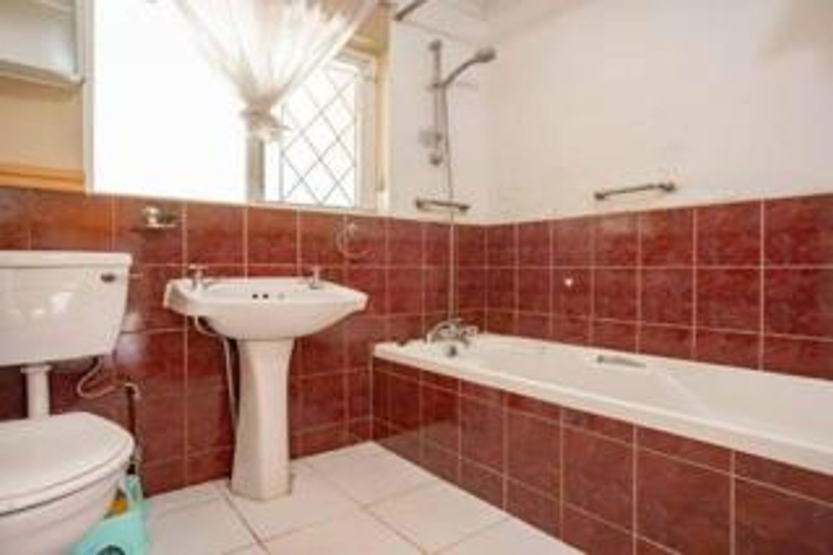 A dated bathroom featuring a pedestal washbasin, bathtub with shower mixer, and full-height red wall tiling.