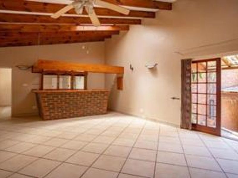 Spacious interior area featuring a built-in brick bar, exposed timber ceiling beams, and direct access to an outdoor patio through a glass door.