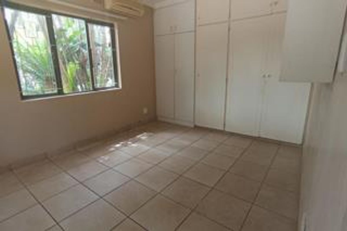 A vacant bedroom featuring neutral tiled flooring, built-in storage cupboards, and an installed air conditioning unit.