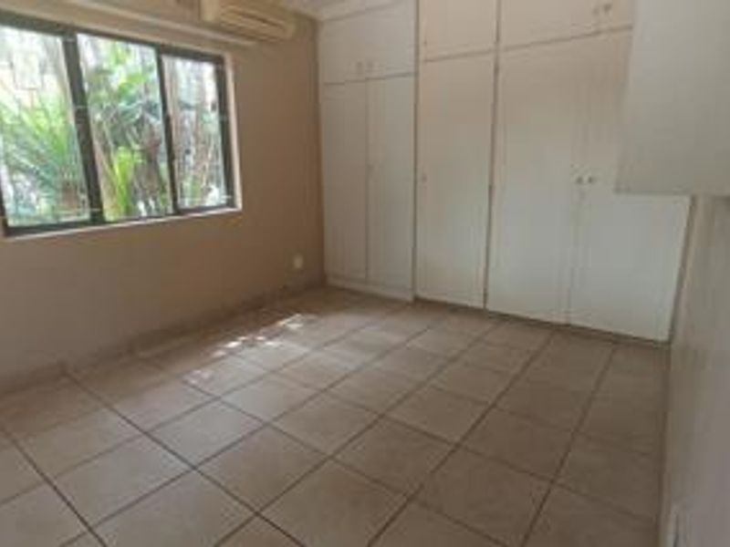 A vacant bedroom featuring neutral tiled flooring, built-in storage cupboards, and an installed air conditioning unit.