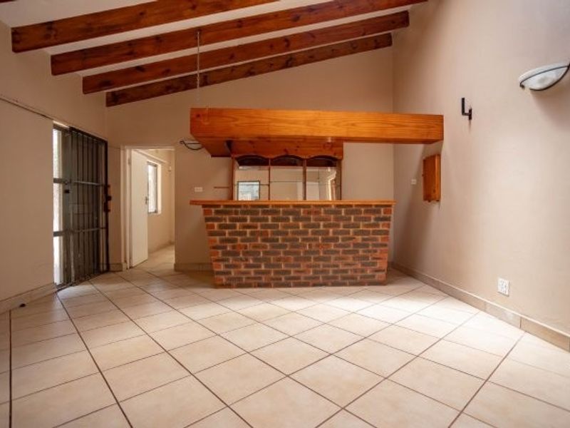 An empty bar area featuring a brick counter, timber canopy, exposed wooden ceiling beams, and tiled flooring, offering potential for a dedicated entertainment space.