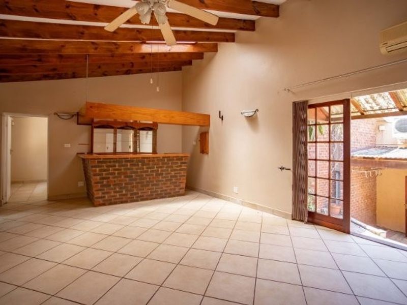 Spacious living area featuring exposed timber beams, a built-in brick bar, tiled flooring, and direct access to an outdoor patio area.