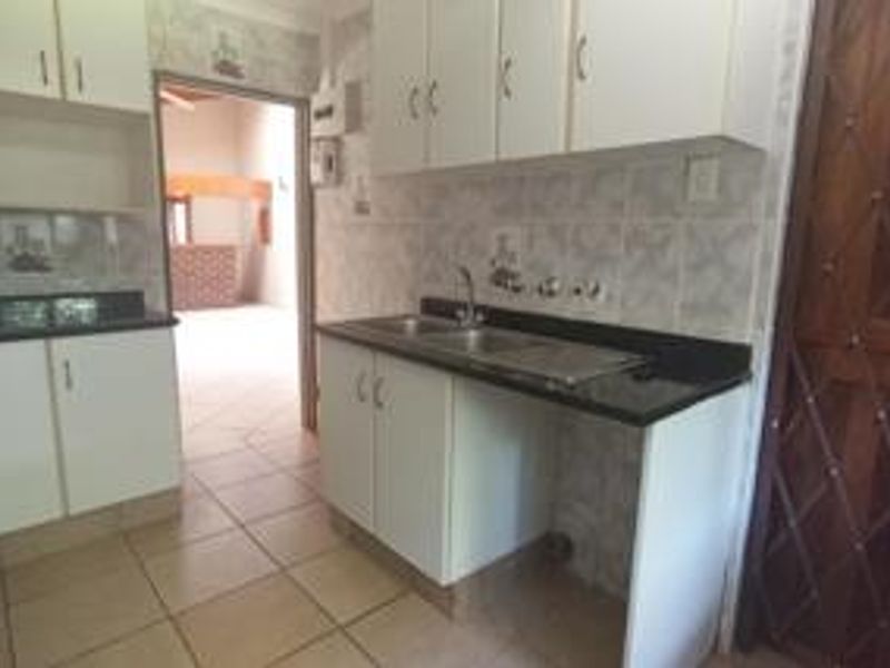 A functional kitchen featuring white built-in cabinetry, granite countertops, and a double sink, with tiled flooring and backsplash throughout.
