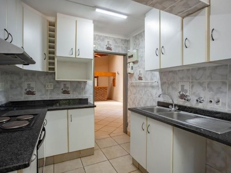 A functional kitchen featuring white cabinetry, granite countertops, a double sink, and an electric hob, with tiled walls and flooring throughout.