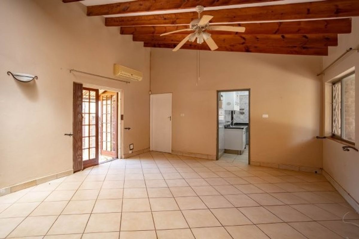Spacious living area featuring exposed timber ceiling beams, ceramic tiled flooring, and direct access to an outdoor area through french doors.