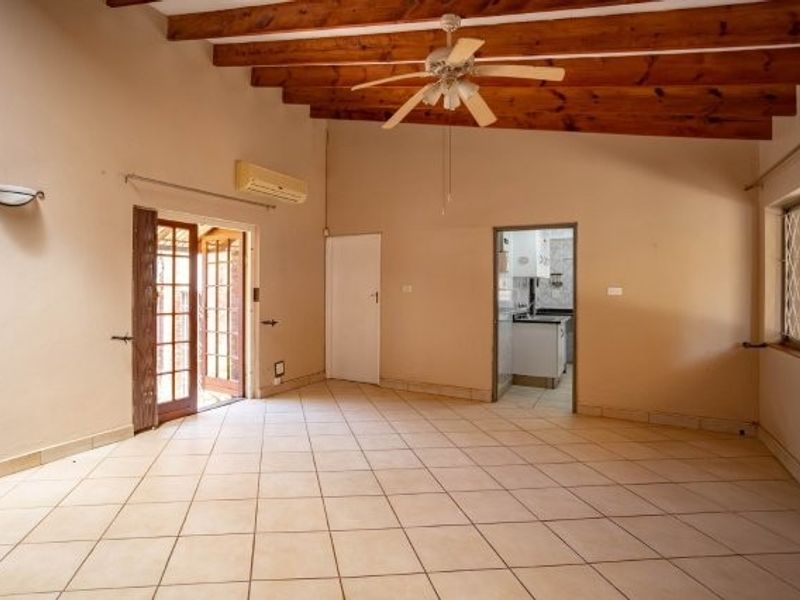 Spacious living area featuring exposed timber ceiling beams, ceramic tiled flooring, and direct access to an outdoor area through french doors.