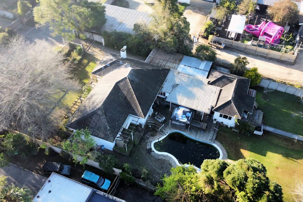 Aerial view of the property featuring a swimming pool, timber decking, and a multi-pitched tiled roof structure set within a residential plot.