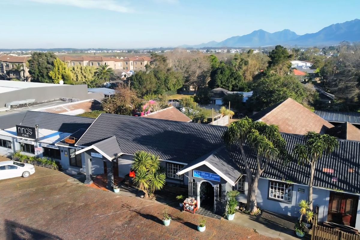 Aerial view of a commercial property complex featuring multiple units, tiled roofing, and a paved parking area with surrounding greenery.