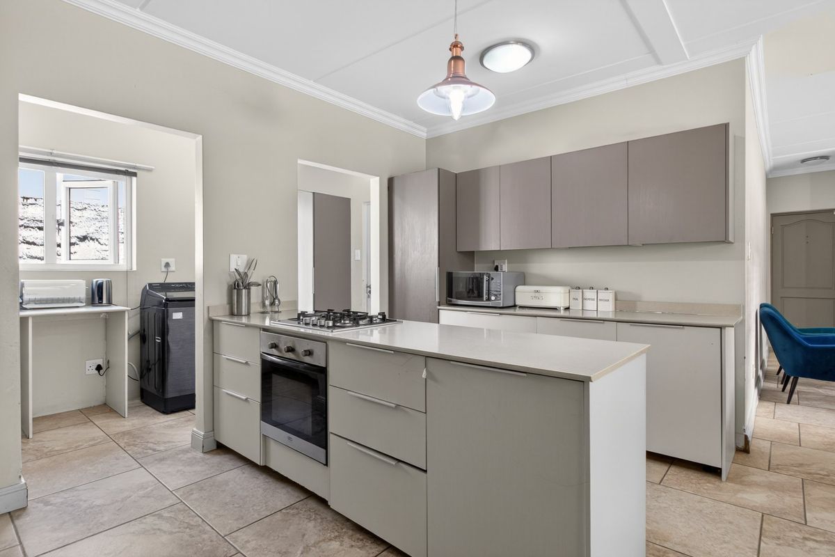 Modern kitchen featuring sleek cabinetry, stone countertops, a gas hob, built-in oven, and tiled flooring, with an adjacent laundry area.