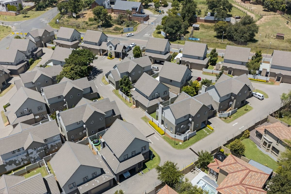 An aerial view of a residential housing complex featuring multiple detached homes with tiled roofs, paved driveways, and established landscaping.
