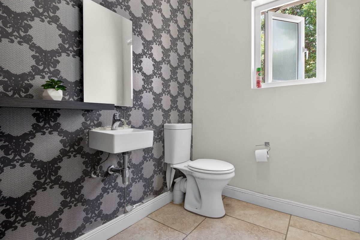A compact guest bathroom featuring a wall-mounted basin, toilet, tiled flooring, and decorative wallpaper.