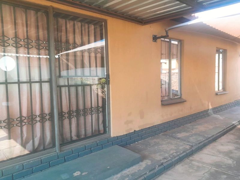 A covered outdoor patio area featuring a sliding glass door with security gate, brick plinth detailing, and concrete paving.