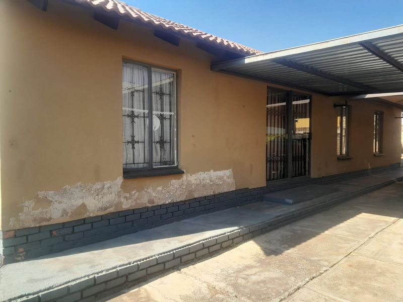 Front exterior view of the house featuring a carport, security bars on windows, and visible signs of rising damp and exterior wall maintenance required.