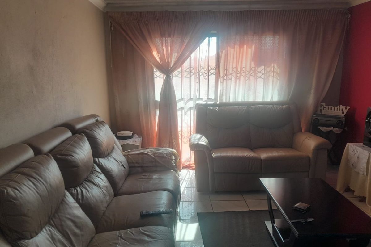 A living room featuring tiled flooring and a sliding door with security gate, requiring cosmetic updates to wall finishes.