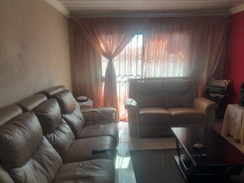 A living room featuring tiled flooring and a sliding door with security gate, requiring cosmetic updates to wall finishes.