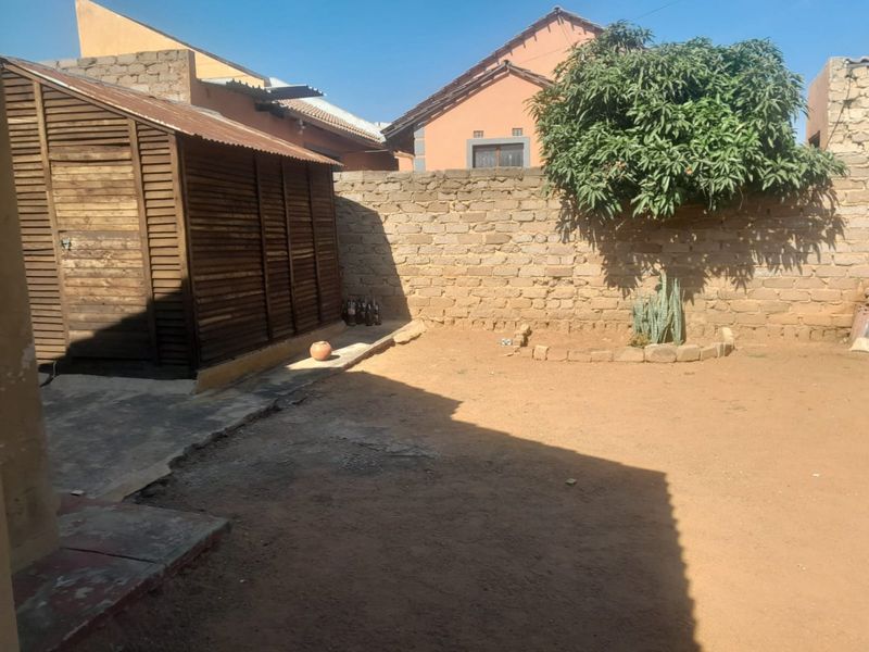 Rear yard area featuring a brick boundary wall, concrete paving, and a wooden storage shed in a basic, unlandscaped setting.
