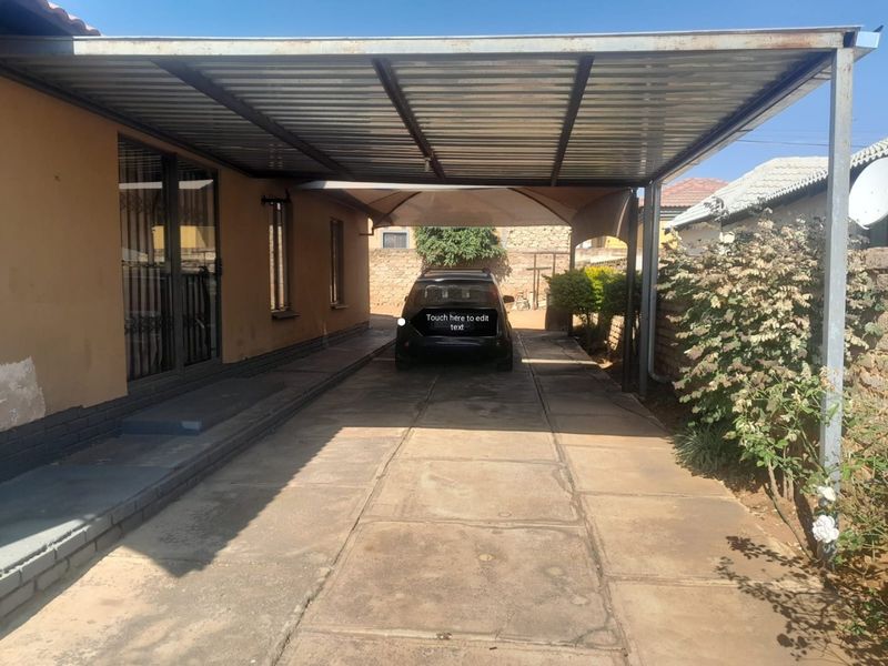 A covered carport area with a metal roof structure and concrete paved driveway, providing sheltered off-street parking.