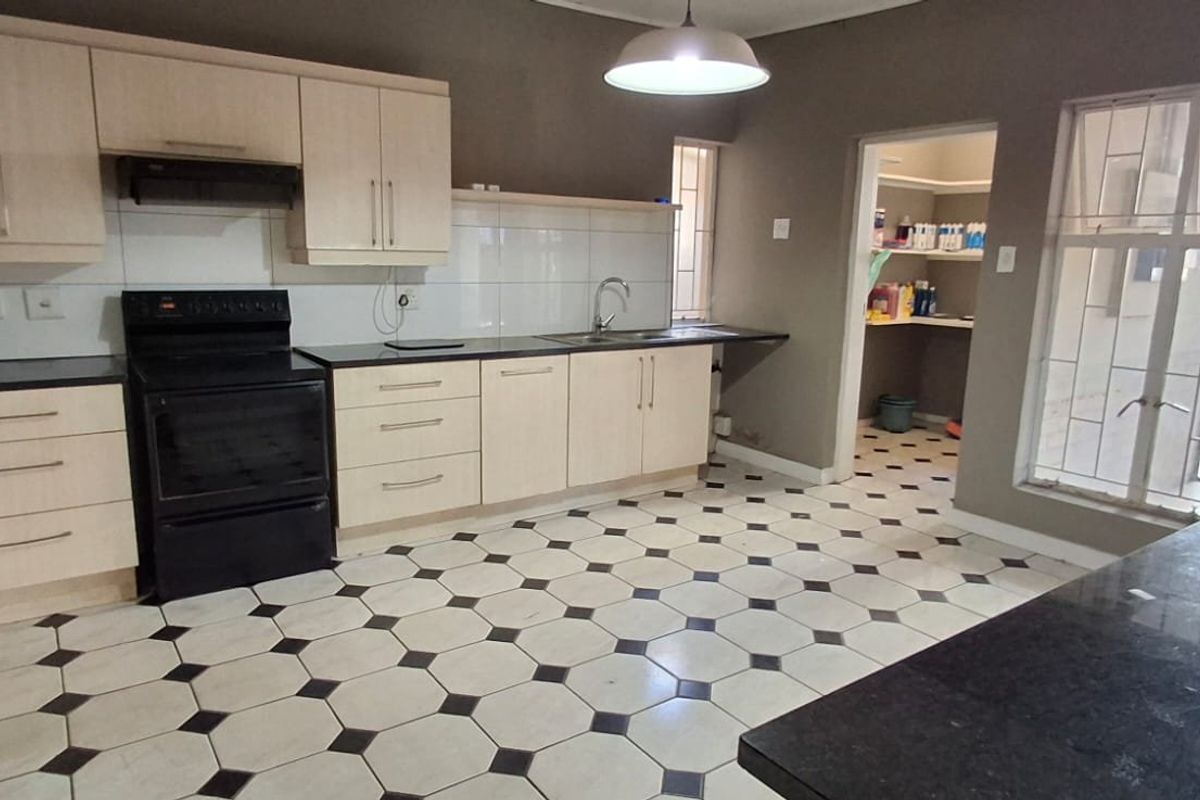 A functional kitchen featuring light-toned cabinetry, dark granite countertops, a freestanding stove, and a tiled floor, with an adjacent scullery area.