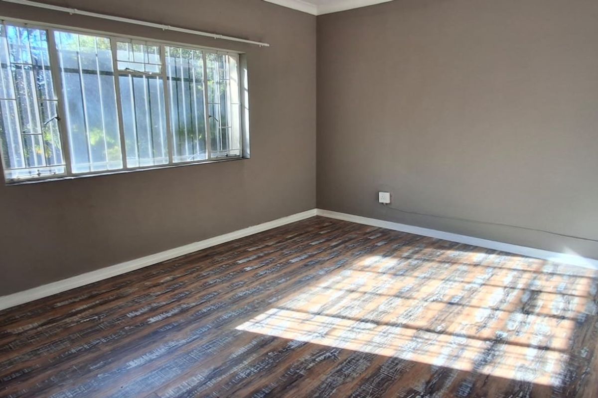 A vacant bedroom featuring wood-look laminate flooring, neutral wall paint, and a window fitted with security bars.