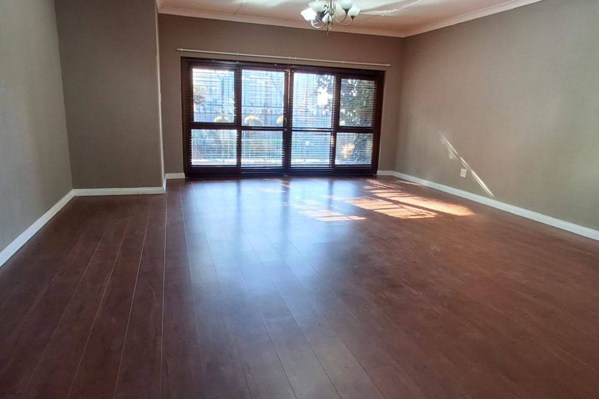 A spacious, empty living room featuring dark laminate flooring, neutral walls, and large sliding glass doors that provide natural light.