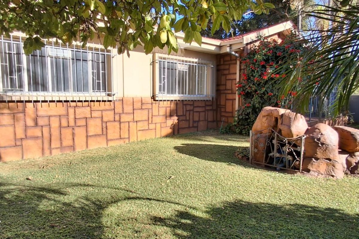 Rear garden area featuring a swimming pool, rock water feature, and a house exterior with stone-cladding detail and security bars on windows.