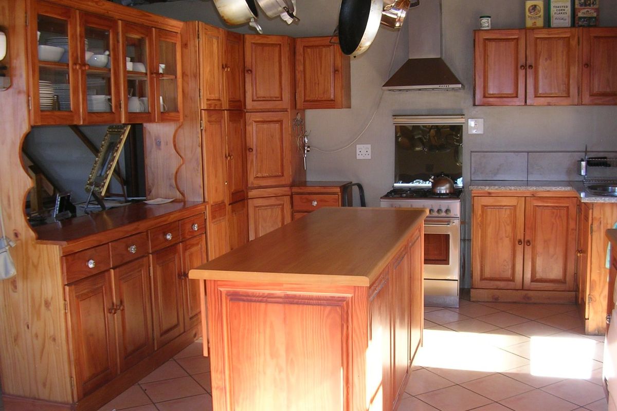 A rustic kitchen featuring extensive wooden cabinetry, a central island, tiled flooring, and a freestanding stove with an extractor fan.