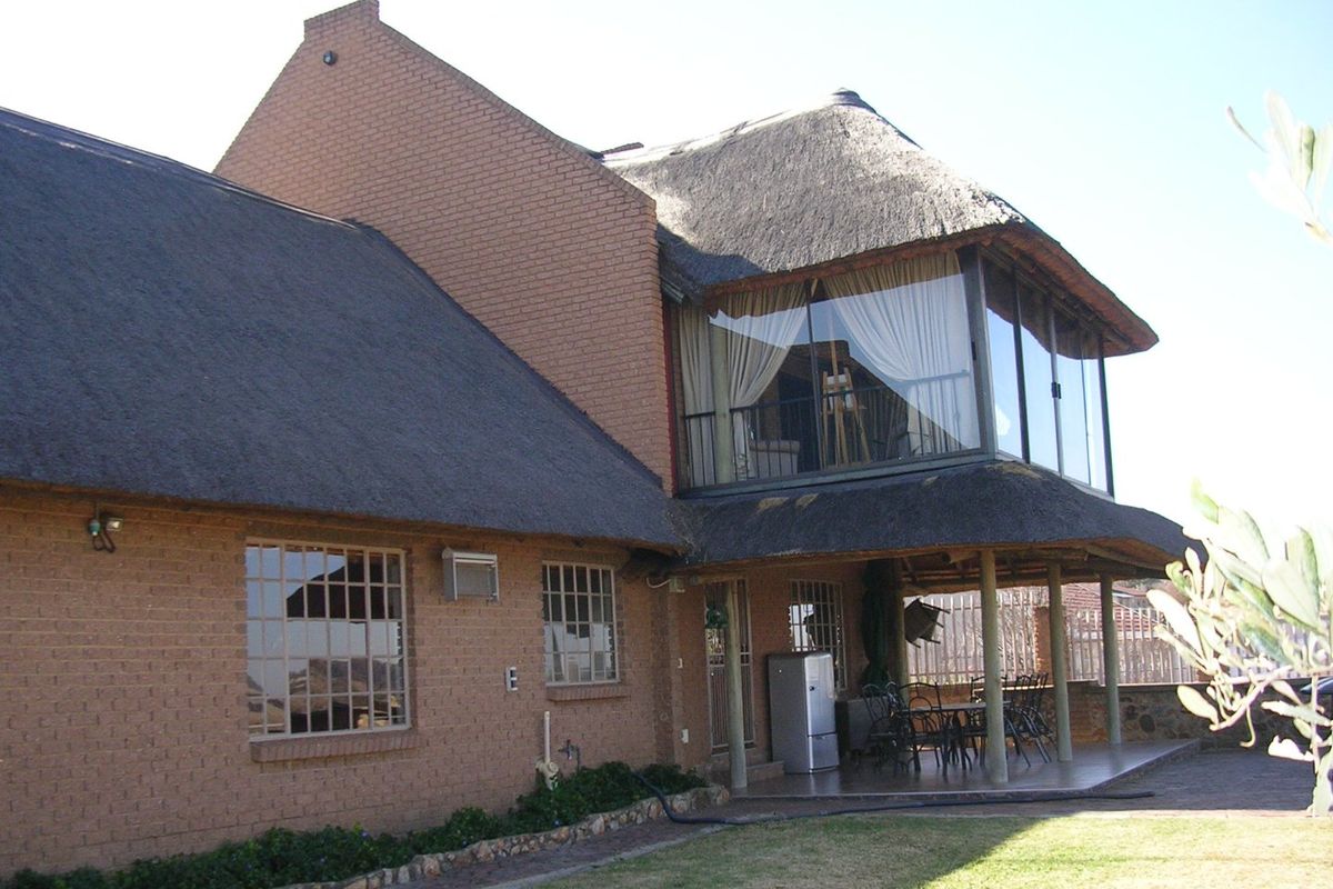Rear view of a two-story brick house featuring a traditional thatch roof, a covered patio area, and an upper-level balcony with large glass windows.