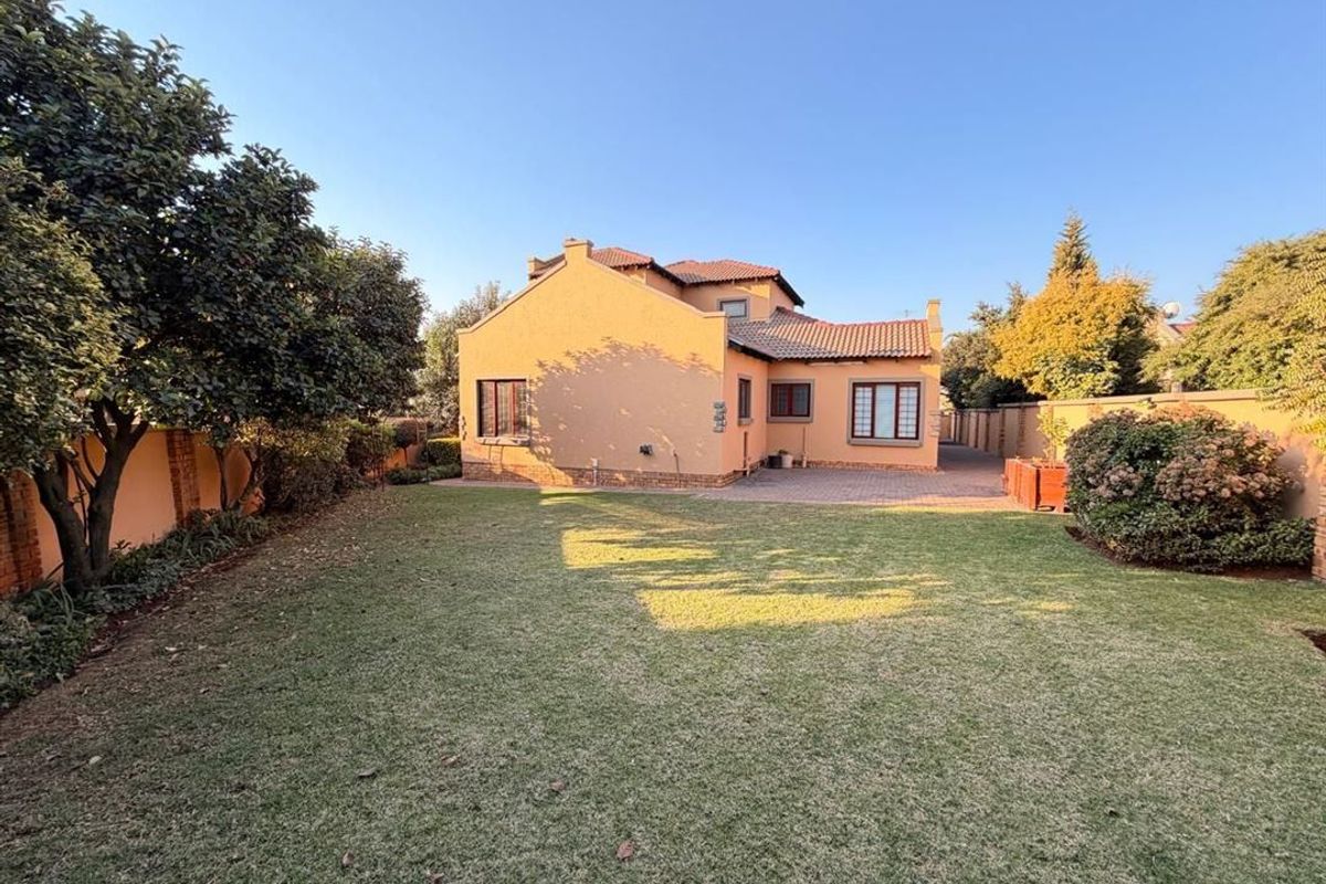 A spacious rear garden featuring a well-maintained lawn, paved patio area, and secure boundary walls, providing a private outdoor space for the townhouse.