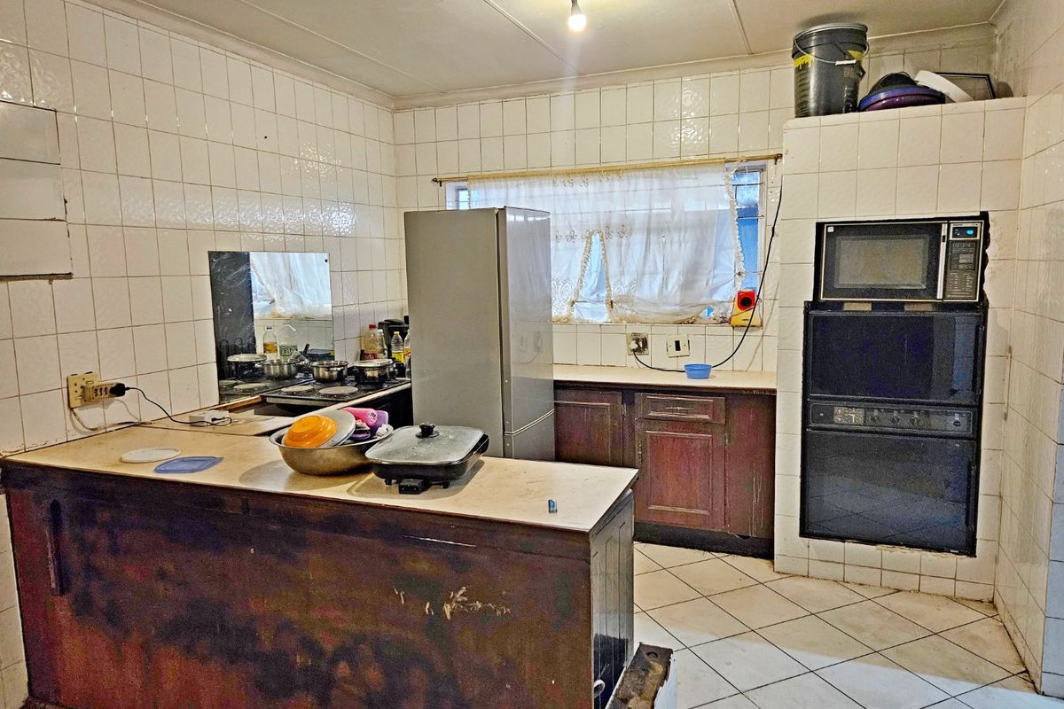 A dated kitchen featuring tiled walls and floors, built-in oven and microwave, and worn cabinetry, offering significant potential for a modern renovation.
