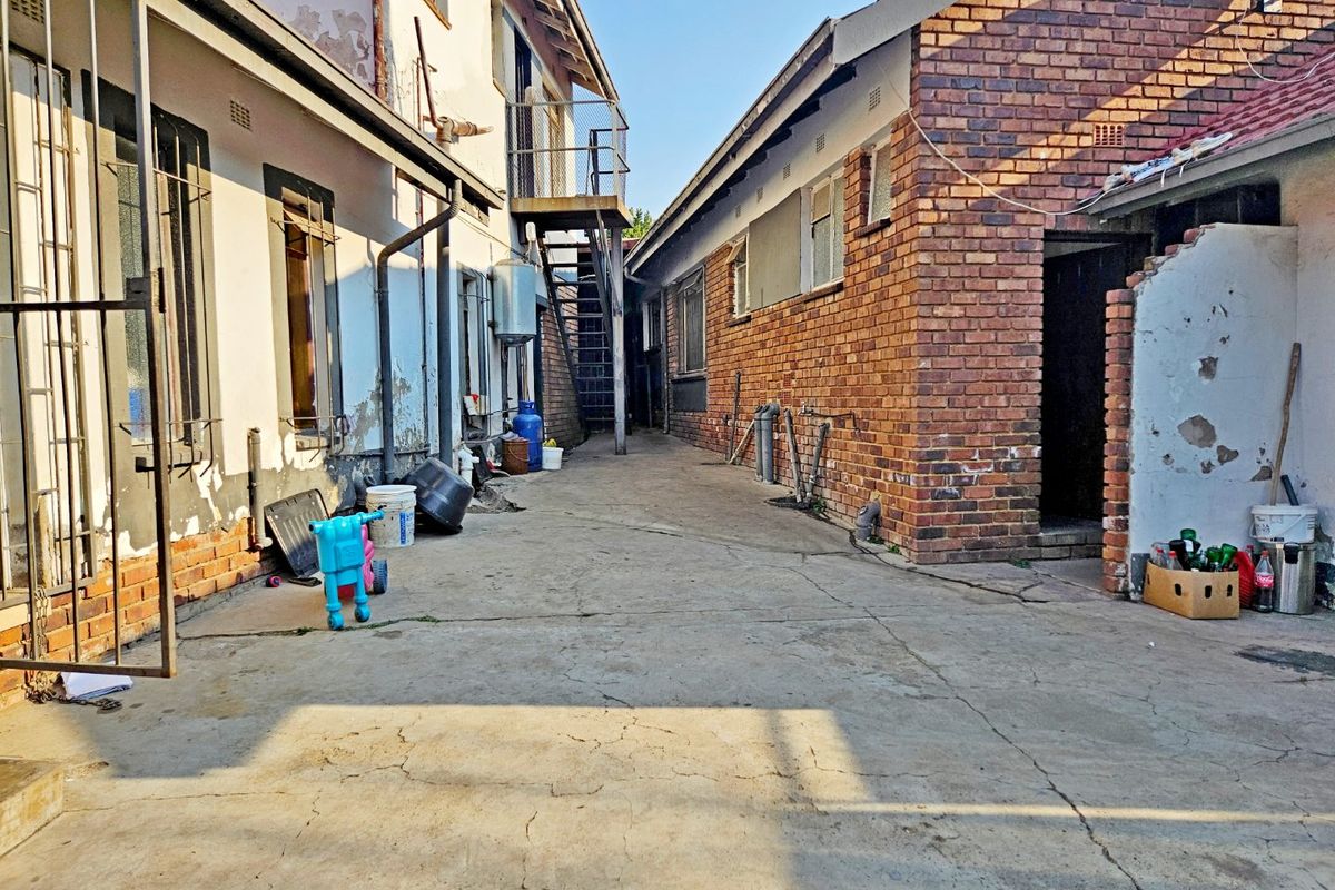 Rear exterior courtyard area featuring concrete paving, brick walls, and an external metal staircase, showing signs of significant wear and maintenance requirements.