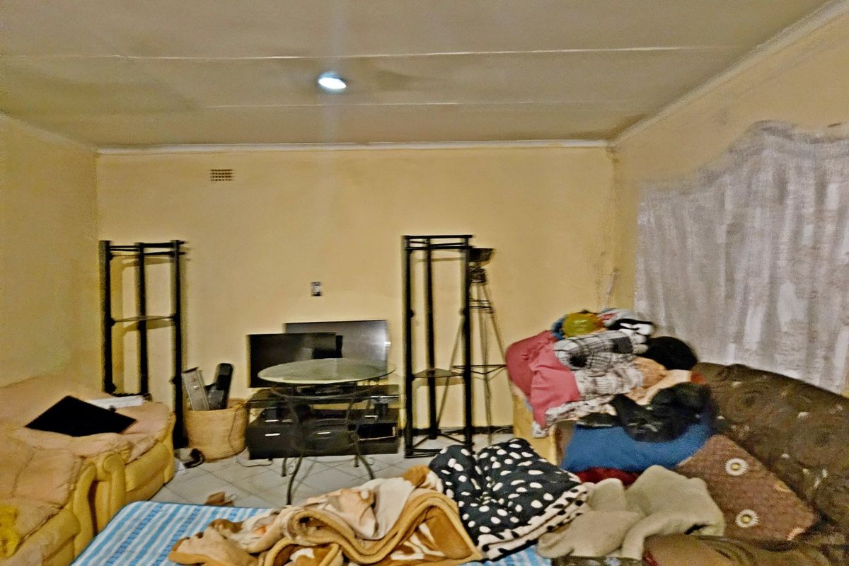 A living room space featuring tiled flooring and a ceiling vent, currently requiring cosmetic updates and wall repairs.