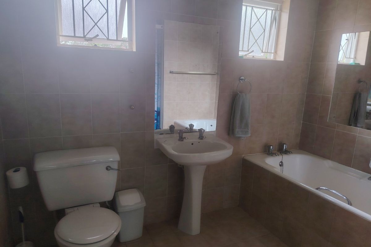 A functional bathroom featuring a pedestal washbasin, a built-in bathtub, and a toilet, finished with neutral wall and floor tiling.