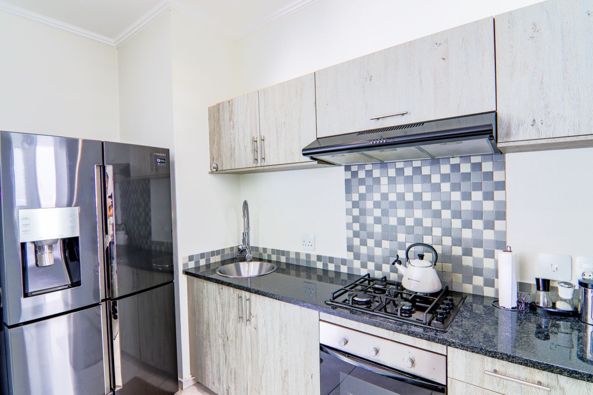 Modern kitchen featuring light wood-grain cabinetry, granite countertops, a gas hob with extractor fan, and a tiled backsplash.