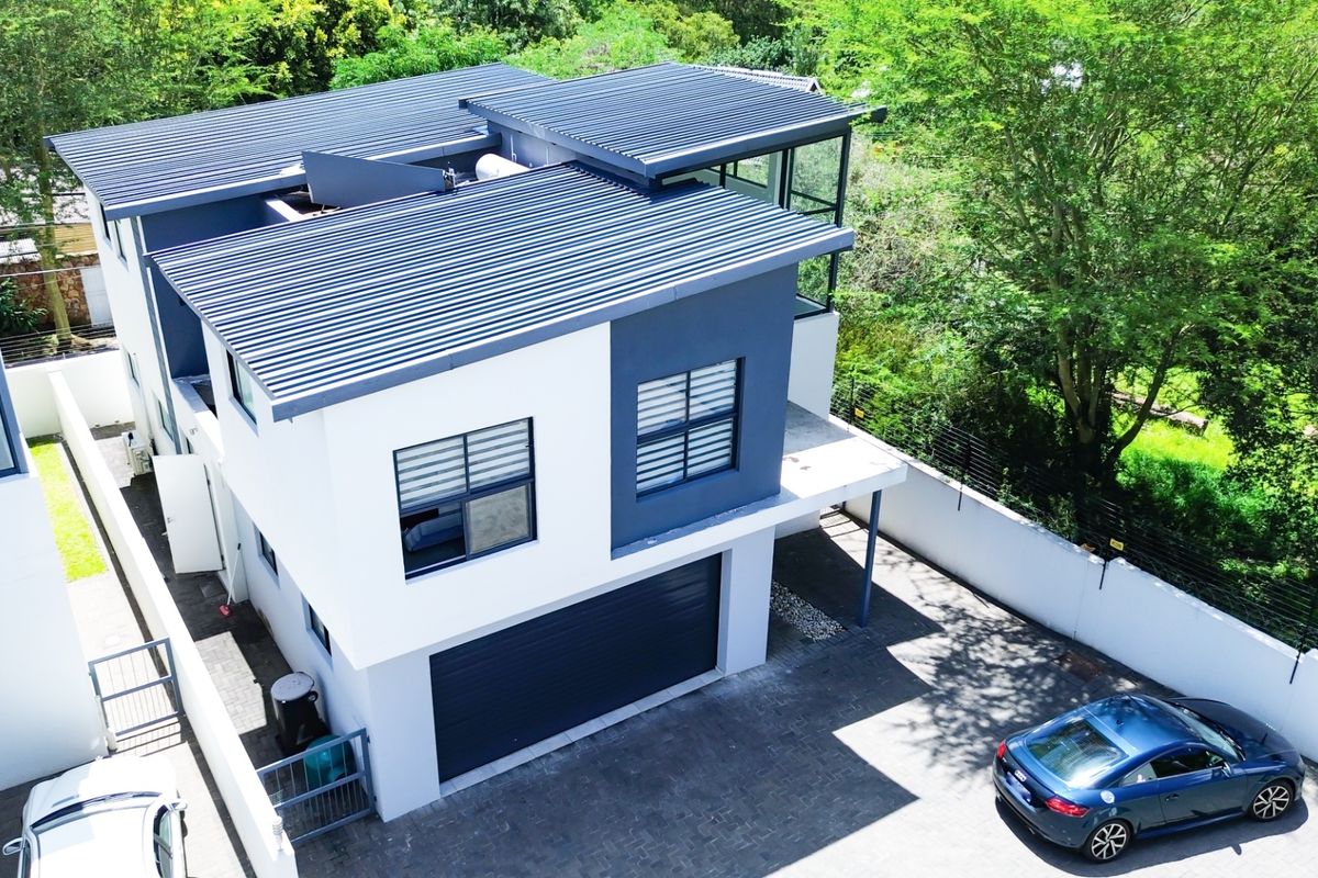 Aerial view of a modern two-story residential property featuring a corrugated metal roof, paved driveway, and secure perimeter wall.