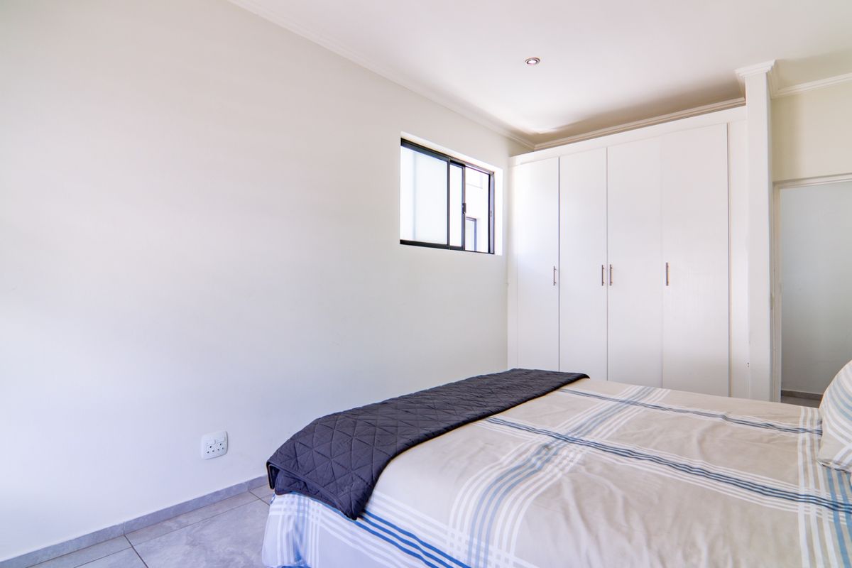A clean, neutral bedroom featuring built-in cupboards, tiled flooring, and a recessed downlight, offering a bright and functional living space.