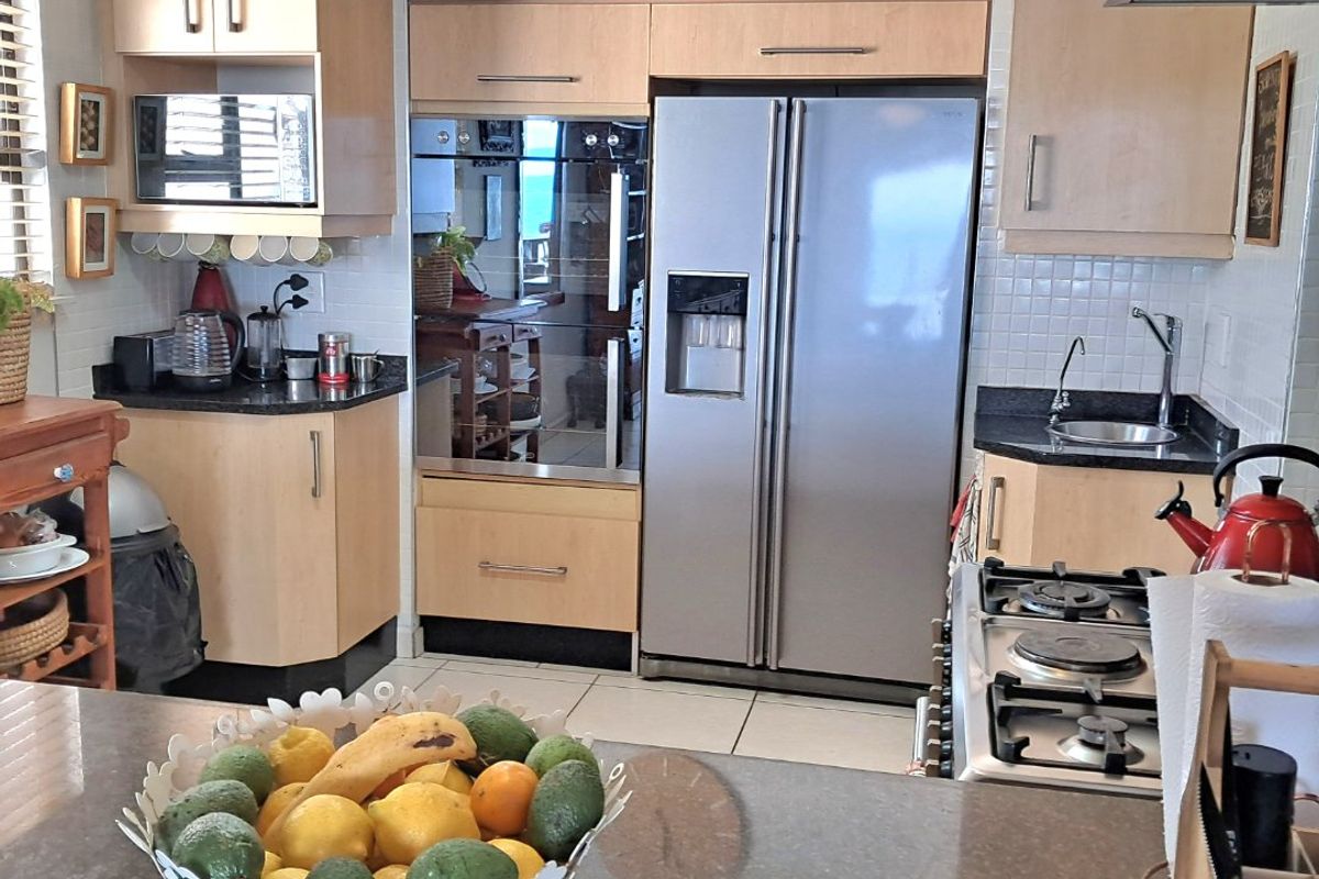 A functional kitchen featuring light wood cabinetry, granite countertops, a gas hob, and integrated appliances, offering a practical layout for daily cooking.