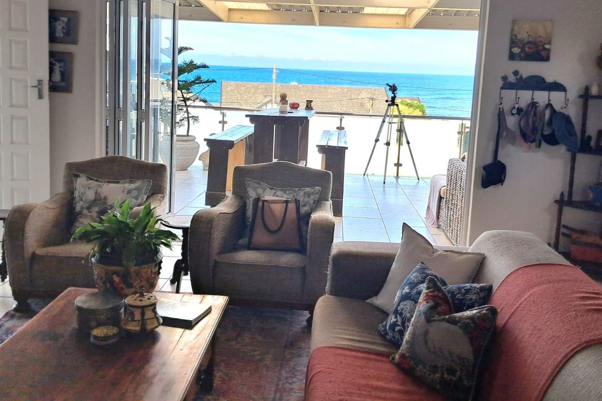 Living room featuring large bi-fold doors opening onto a tiled patio with ocean views and a stainless steel balustrade.