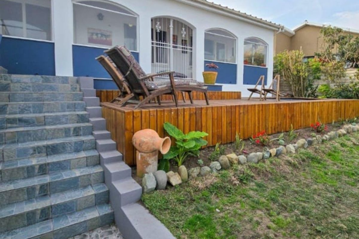 Rear exterior view featuring a raised timber deck, tiled staircase, and arched windows leading into the home, set against a garden area.